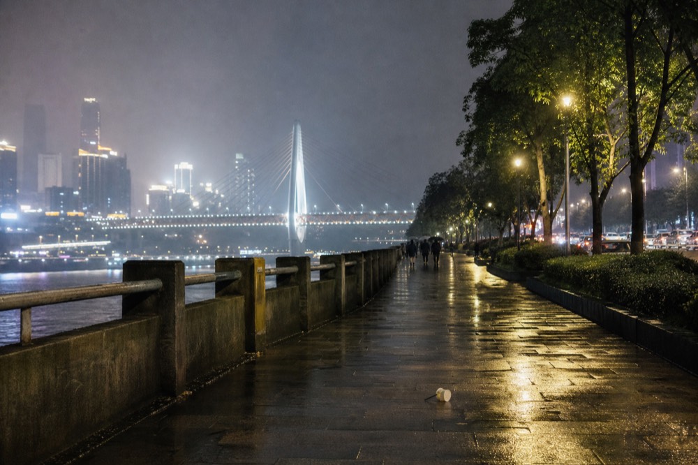 Riverside promenade at night with a lit bridge and distant illuminated high-rises