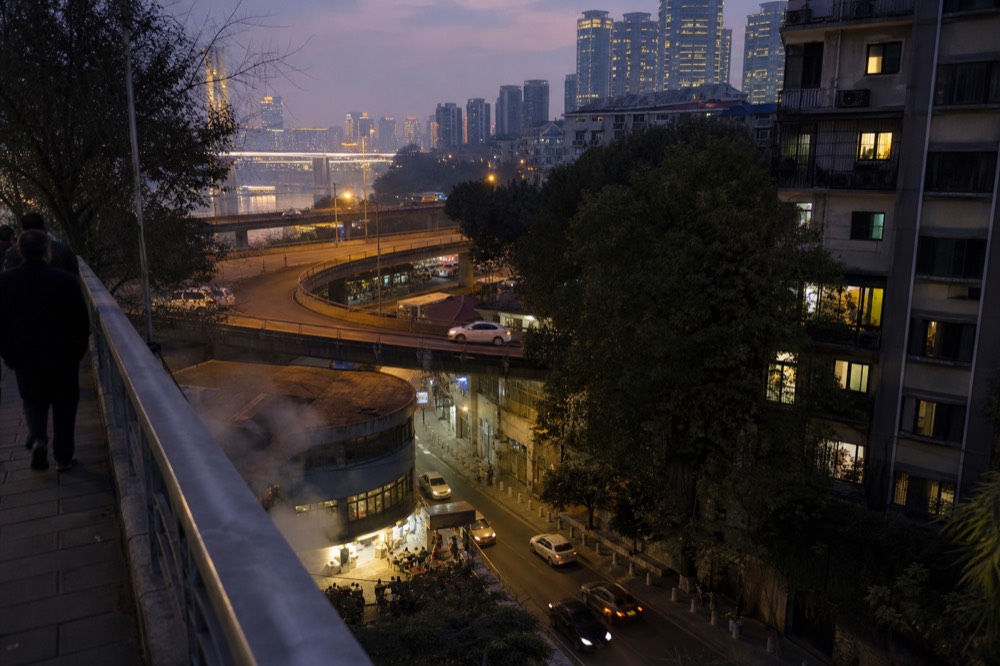 A pedestrian bridge above multi-level city streets at dusk with lit signage