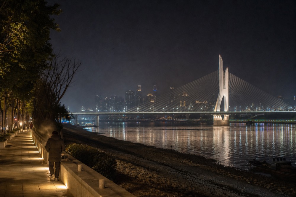 Lit cable-stay bridge towers rising over dark water with city lights beyond