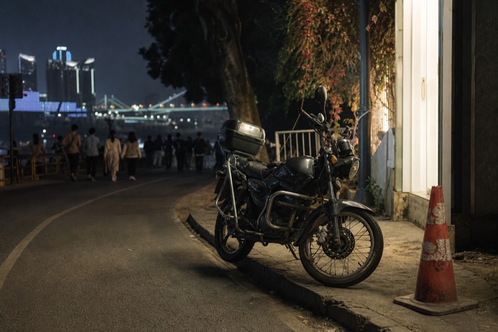 Night city street with glowing signs and a motorcycle parked by the kerb