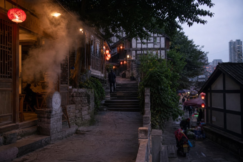 A narrow traditional shopping street lit by red lanterns with stone steps rising between old buildings