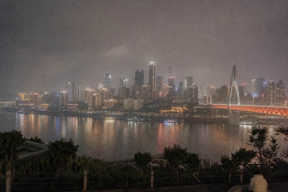 A city skyline across a wide river at night with towers lit and reflections on the water
