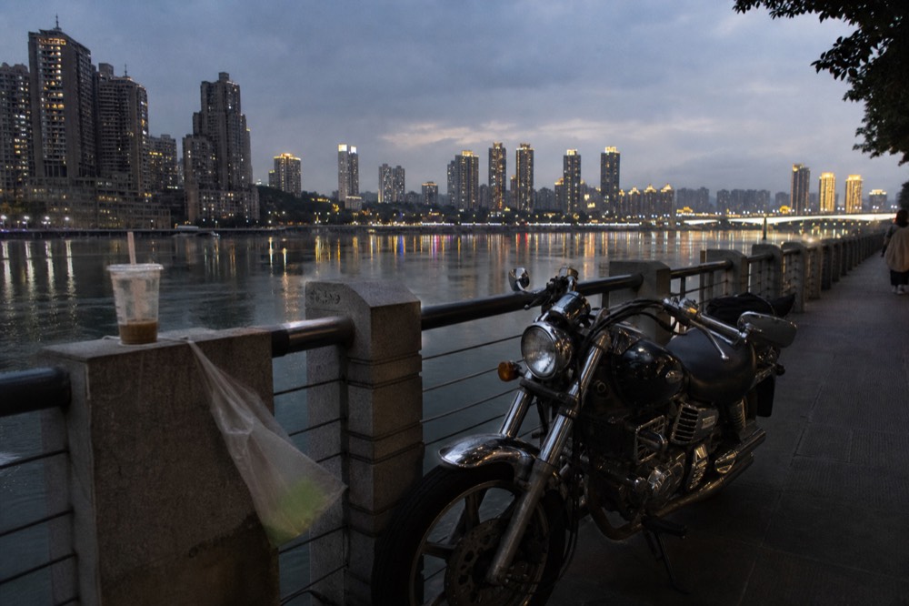 Motorcycle parked on a riverside promenade at night with city lights in the background
