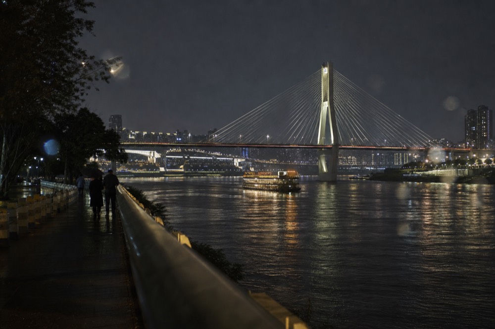 A lit cable-stayed bridge spanning a wide river with illuminated towers along both banks at night