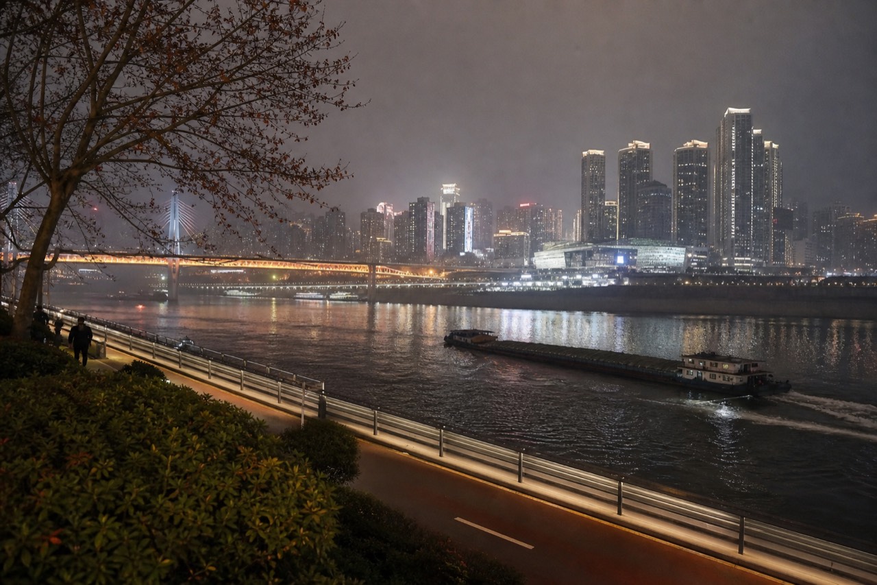 Illuminated high-rise towers and bridges rising above a dark river in central Chongqing at night