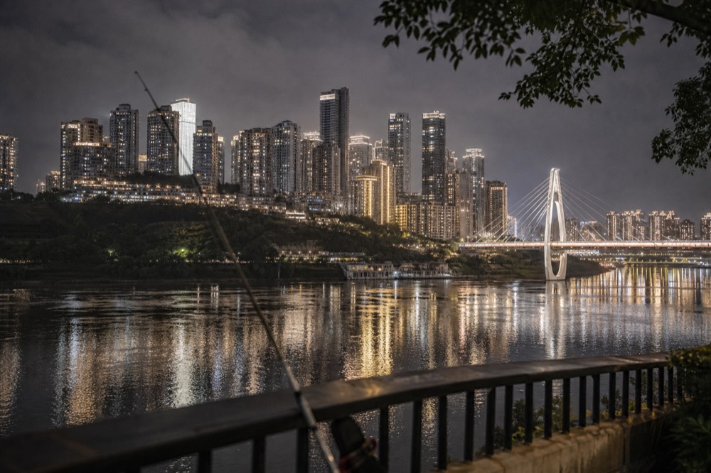 Night view across a wide river toward a dense cluster of illuminated towers and a lit cable-stay bridge