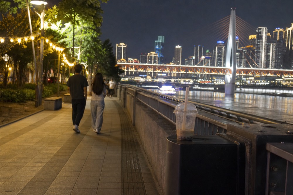 Riverside promenade in Chongqing at night with the lit bridge and tower skyline across the dark water