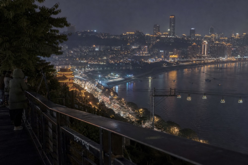 Night panorama of a hillside city with lights rising in tiers above a dark river