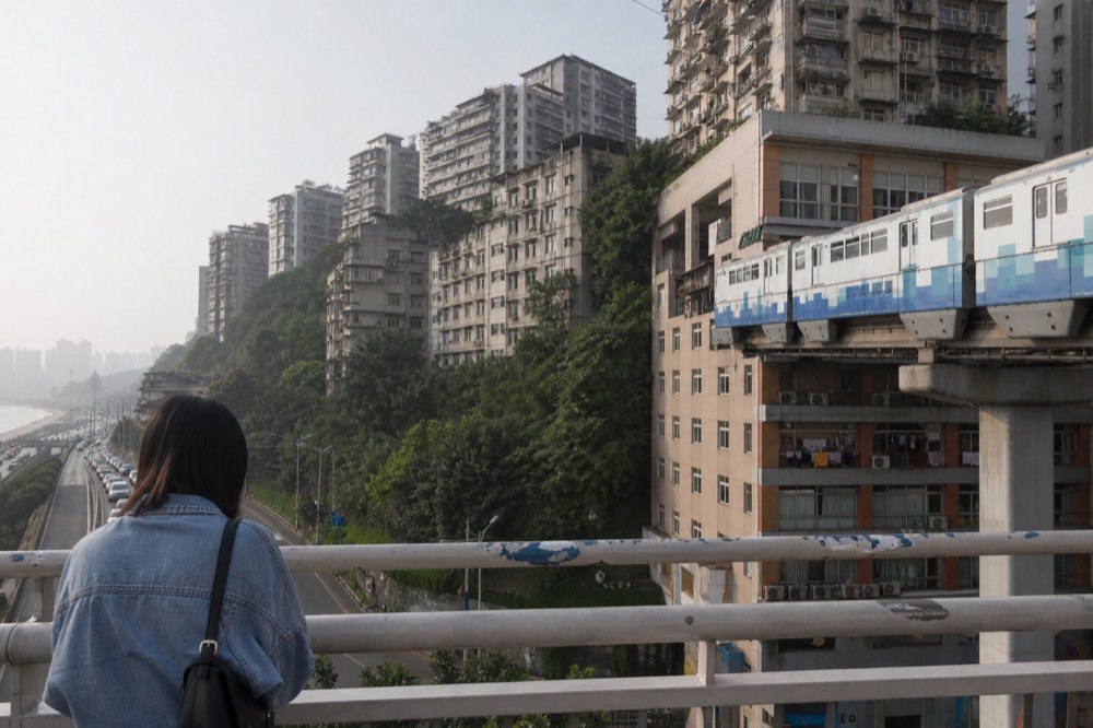 Elevated monorail track curving between residential apartment towers in a dense hillside city