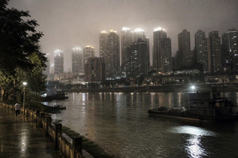 A night skyline of dense high-rise buildings glowing above a dark river, seen from across the water