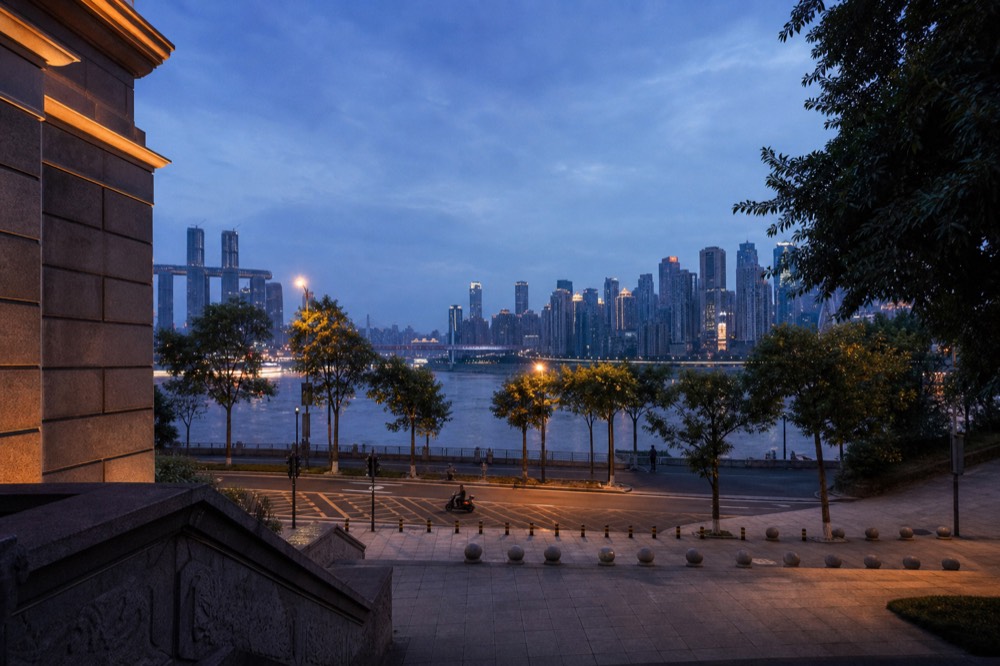 Layered city skyline above a river at dusk with deep blue sky