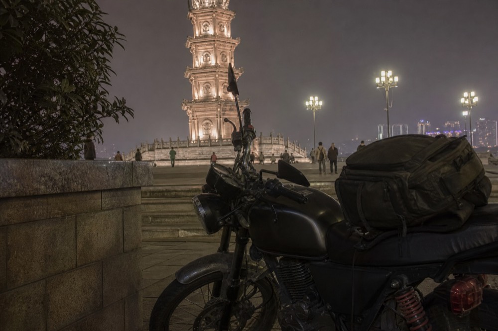 A motorcycle standing under night lights with a camera bag on the seat