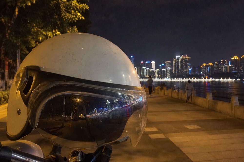 An open-face helmet resting on a motorcycle's handlebars with city lights reflected in its visor