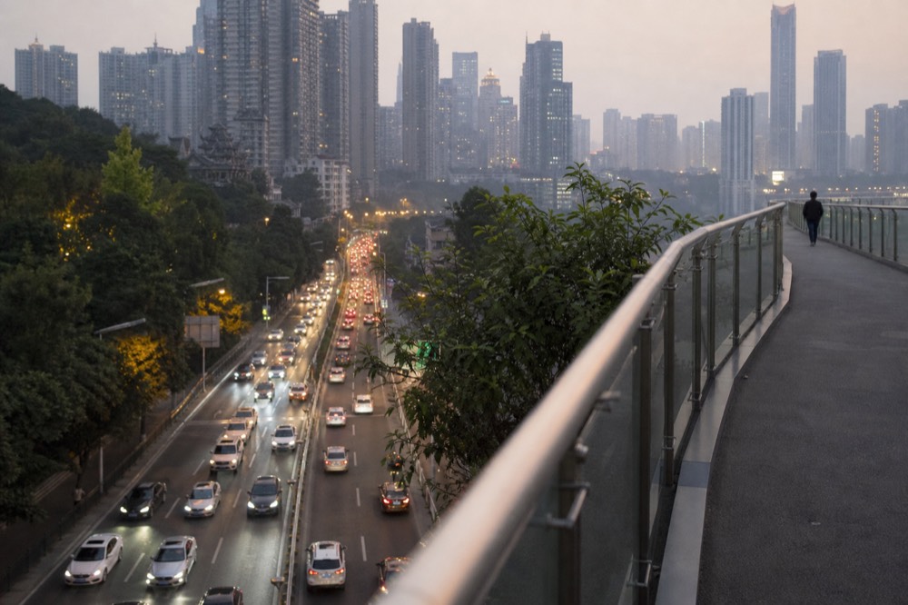 Pedestrian bridge high above a dense city street with illuminated buildings below
