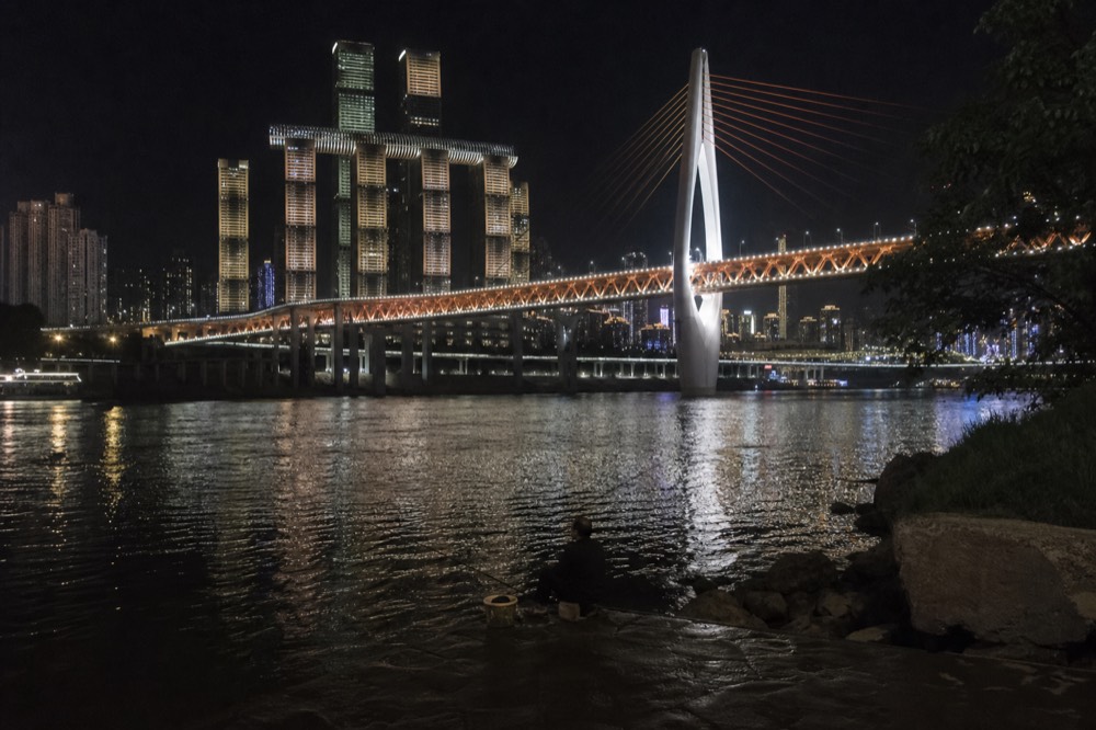 Elevated bridge lit at night above a wide river with city towers behind it