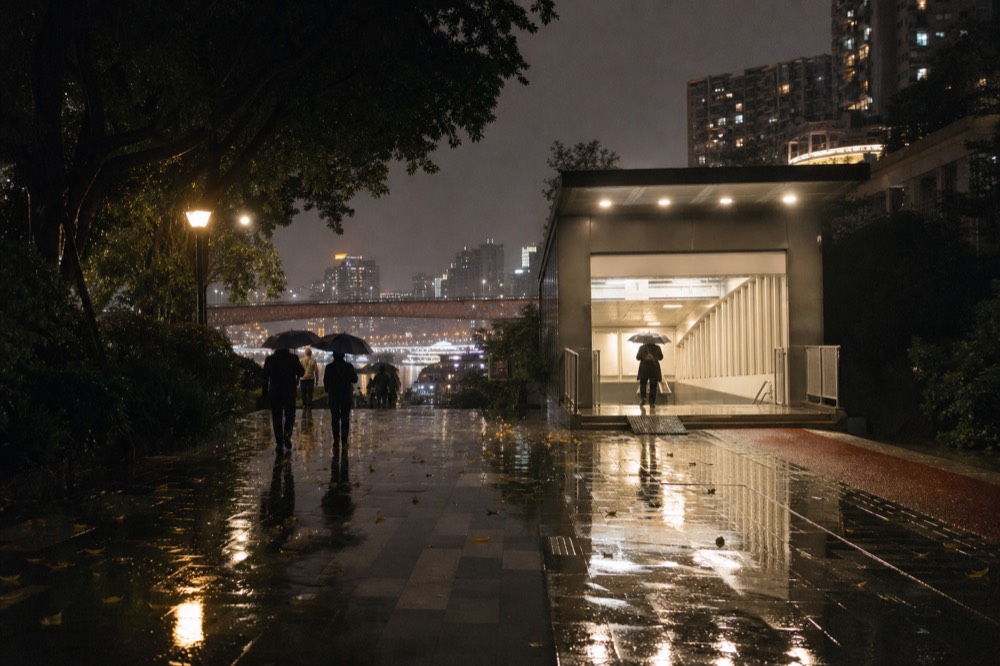Illuminated metro station entrance on a rainy sloping Chongqing street at night