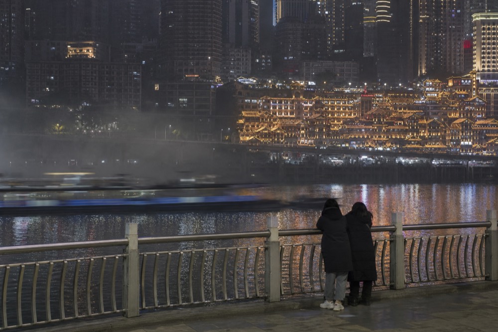 Night view across a river toward an illuminated cliffside building and city towers