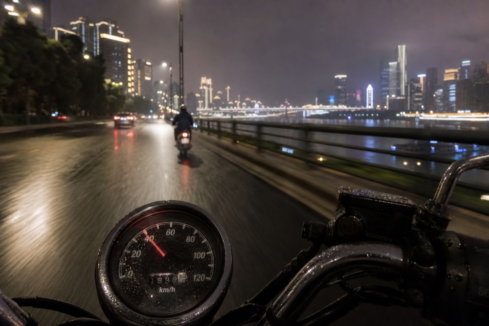 A motorcycle speedometer needle sitting just under 40 km/h with the blurred lights of a city street behind it