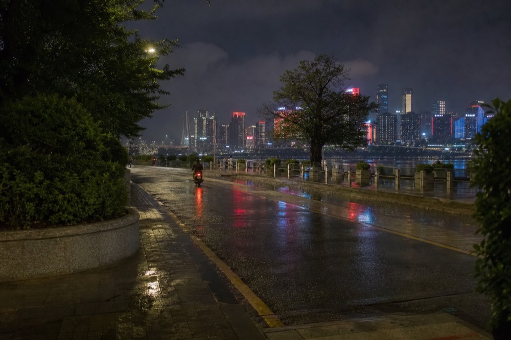 A wet road surface reflecting the neon lights of Chongqing at night, with a motorcycle visible in the distance