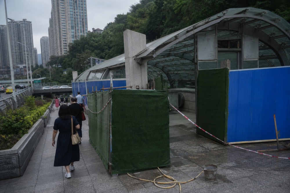 A station entrance partly screened by renovation hoardings with passengers walking past