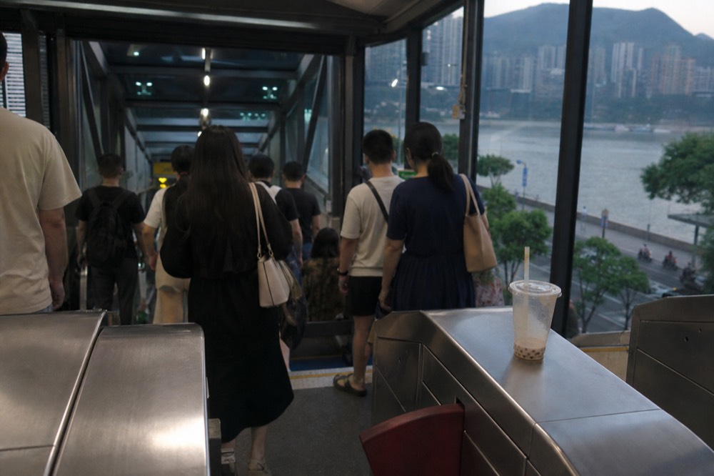 A metro station concourse with fare gates and passengers at the foot of an escalator