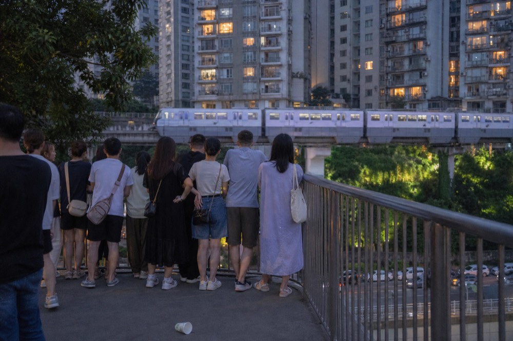 Evening crowd on a Chongqing viewing platform as a monorail passes between lit apartment towers