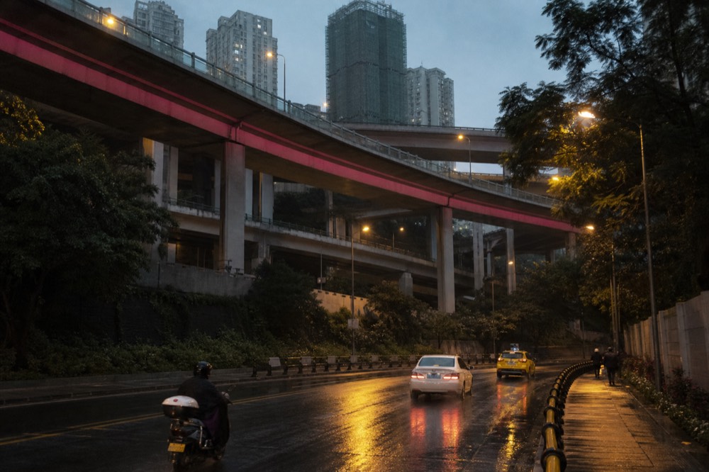 Multi-level elevated roads and bridges crossing above a hilly cityscape at dusk
