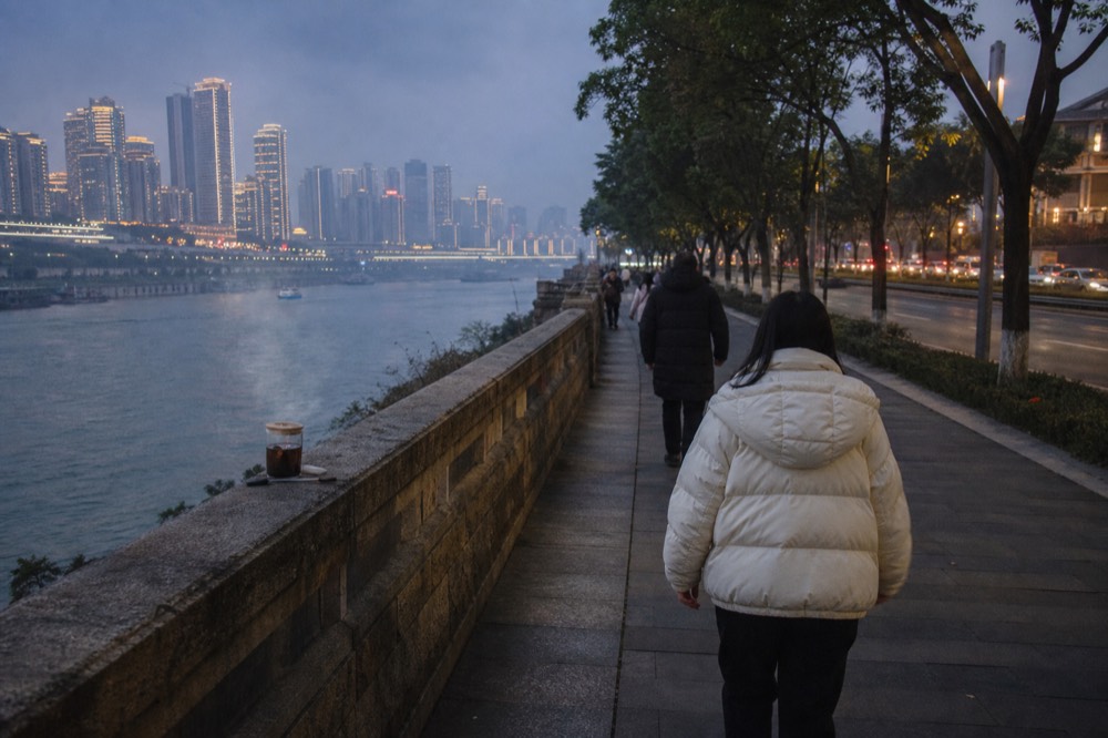 A riverside promenade with lit towers across the water and pedestrians along the railing
