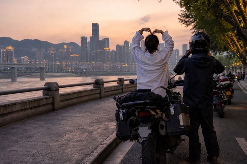 A rider and passenger rehearsing poses on a parked motorcycle along Nanbin Road at sunset