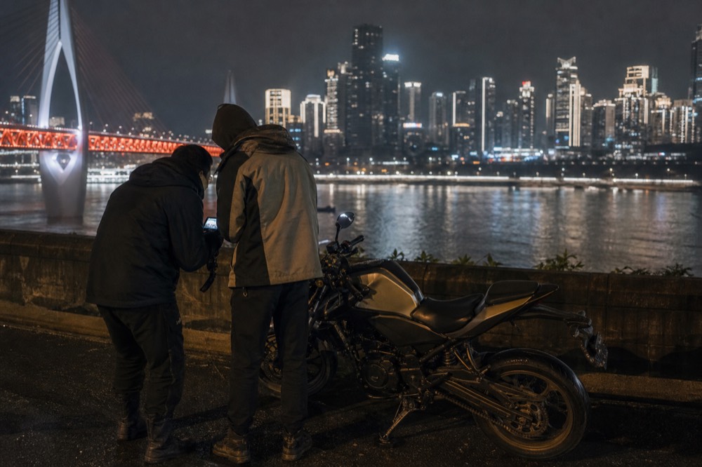 A rider and photographer reviewing footage on a camera screen beside Nanbin Road after a shoot