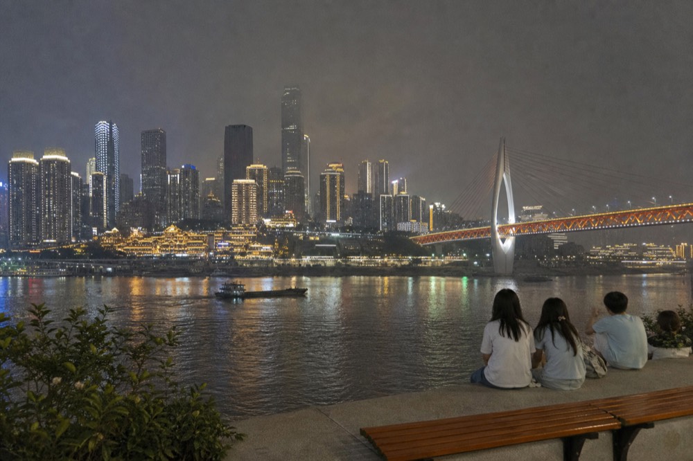 A city skyline of towers and bridges illuminated at night above a dark river