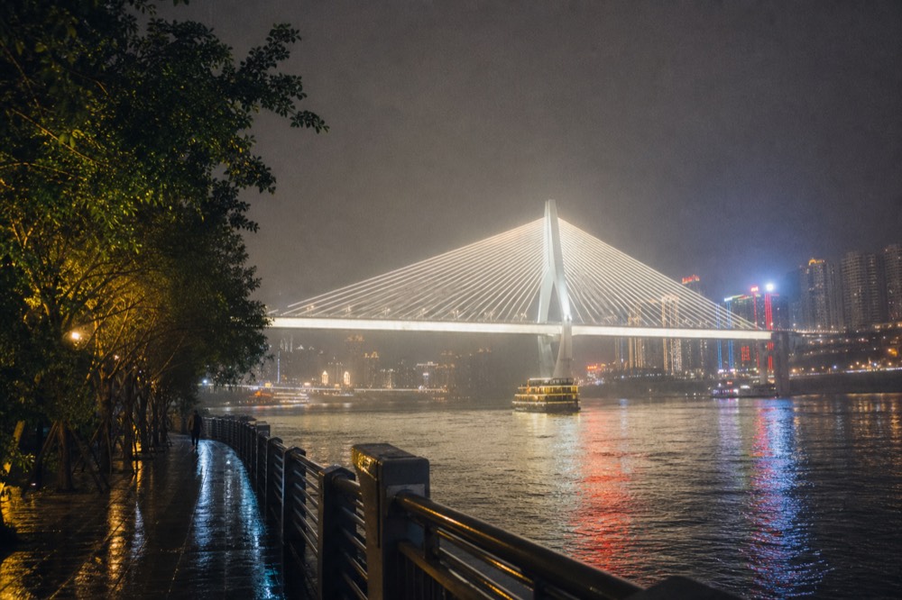 A brightly lit bridge and tower skyline reflecting on a dark river surface