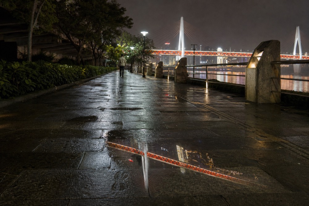 A wet riverside walkway at night reflecting the lights of a bridge