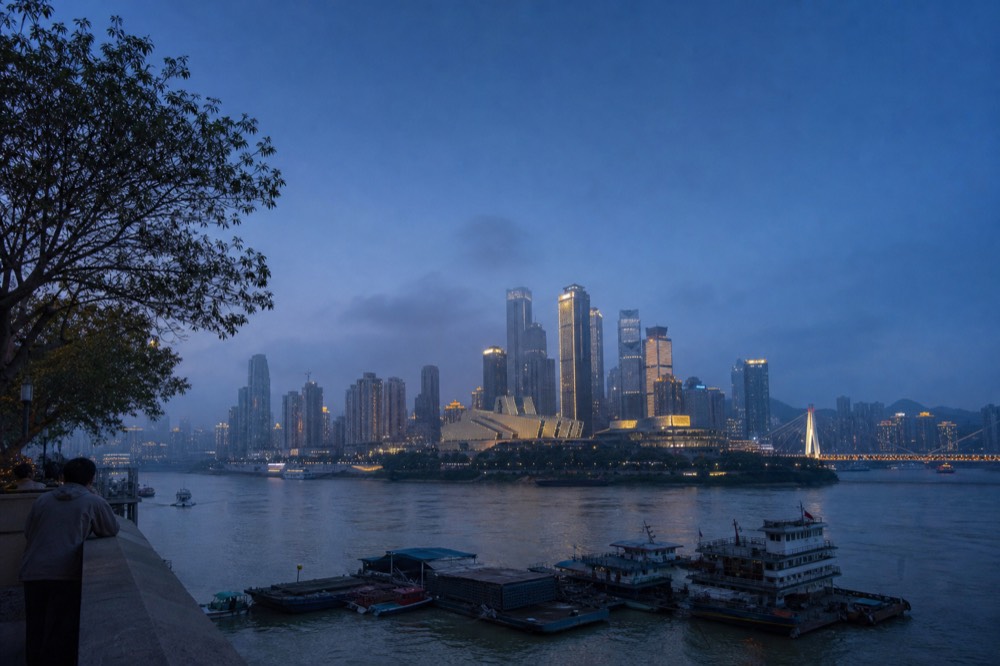 City skyline with lit towers standing against a gradient of deep blue evening sky above a dark river
