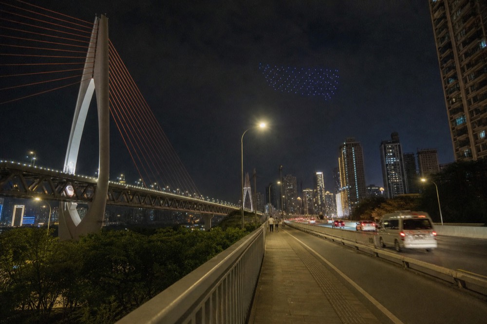 An elevated riverside road at night with street lights and distant bridge cables glowing against a dark sky