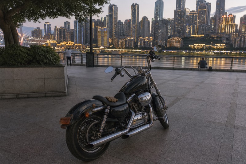 A motorcycle parked at the Chongqing riverside at night with nobody on it, its polished surfaces catching reflections from the skyline across the Yangtze.