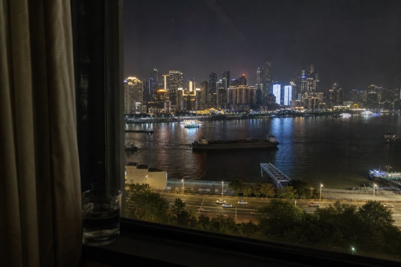 Hotel room windows overlooking the Yangtze in Chongqing at night, the river traffic and the illuminated opposite bank laid out beneath them.