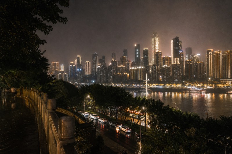 View from the Chongqing south bank after dark, the Yangtze flowing below and the illuminated high-rises of the Yuzhong peninsula stacked along the opposite shore.